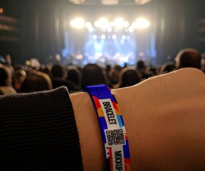 Close-up of a colorful wristband mockup worn at a concert. The blurred stage lights create a vibrant background.