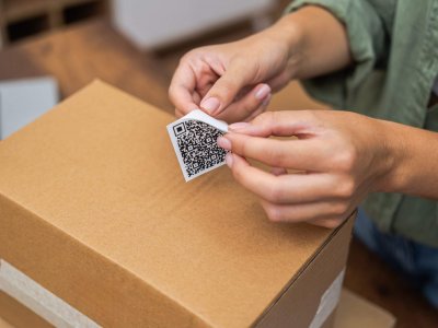 woman hands affix QR code sticker to package, e-commerce delivery and online shopping Close-up: A woman's hands affix a QR code sticker to a package, epitomizing the e-commerce delivery and online shopping experience.